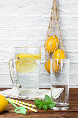 Lemonade with mint in jug, glass and lemons in grid bag on wooden table