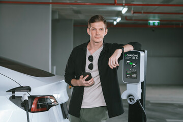 Young man travel with EV electric car to shopping center parking lot charging in downtown city...