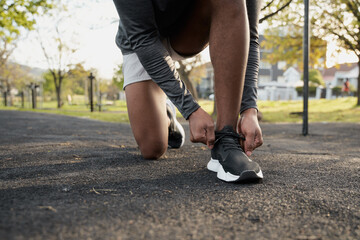 Close-up of young black man in sports clothing kneeling while tying shoelace in park