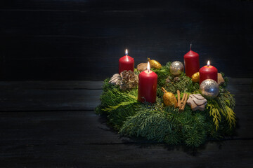 Light in the dark on third advent, natural green wreath with red candles, three are burning,...