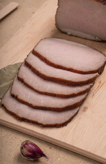 Smoked pork cut into thin slices. Serving on a wooden board on a beige background