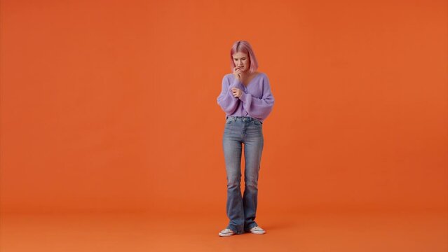 Worried woman nervously walking over orange background