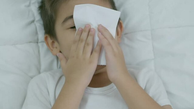Caucasian boy child in bed feeling unwell blowing his nose sneezing symptoms for cold or bronchitis. Healthcare concept. Slow motion. High quality 4k footage