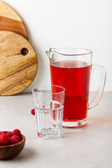 Red color drink in the glass jug on gray background.