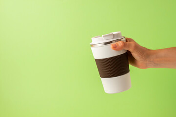 Hand of a girl taking a thermos of coffee on a green background. copy space