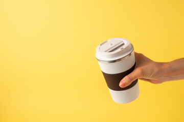 Hand of a girl taking a thermos of coffee on a yellow background. copy space