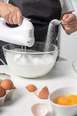 A woman beats eggs with a mixer while adds sugar