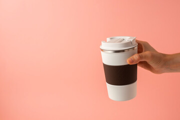 Hand of a girl taking a thermos of coffee on a pink background. copy space