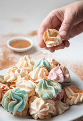 A female hand holds a meringue. On the table a plate of kiss meringues sprinkled with cinnamon on a white table