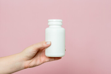 Bottle of pills or vitamins in woman's hand. White packaging for your pill or capsule and supplement