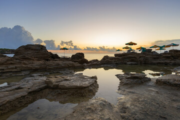 A romantic bay by the sea at sunrise with small lagoons in which the sky is reflected. Among the...