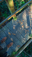 A wooden bridge over a stream strewn with autumn leaves and boots standing on it - 684337643