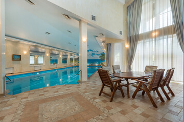 A luxurious mansion with a swimming pool. Exclusive design of the room. Lounge chairs .with a table by the panoramic window.