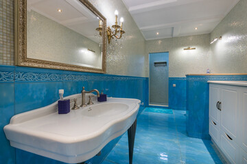 Bathroom with exclusive blue tile finish. A mirror in a gilded frame above the sink. .Stylish accessories.