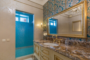 Expensive bathroom interior with silk wallpaper. A mirror in a gilded frame above a .cabinet with a...