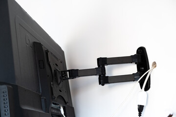 Flat screen TV hanging on a metal mount on the white wall in the room. Black TV bracket, mount...