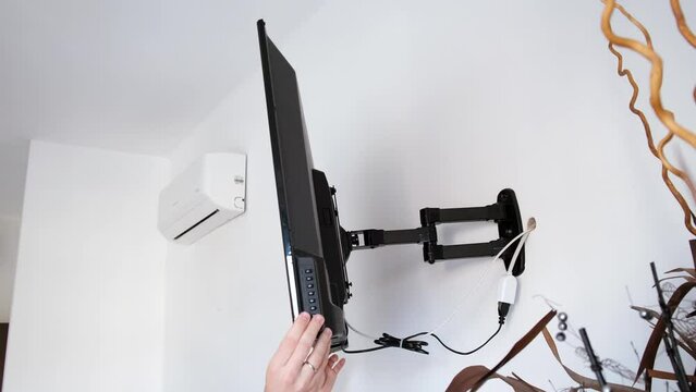 A man rotates a flat-screen TV hanging on a bracket, demonstrating a wide angle of rotation of the screen. The TV bracket demonstration. Mount bracket for LCD monitor, plasma TV, LED display device.