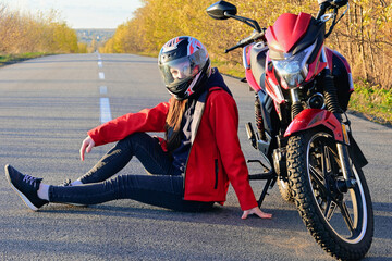 young attractive biker girl in red sitting next to her red motorcycle in the middle of the road....