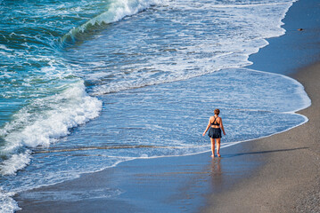 Woman walking on the sand of the beach barefoot at the height of the sea water, elevated view.