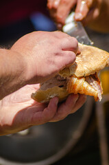 hand holding meat between two pieces of bread to make a Bifana, a typical Portuguese meat sandwich.