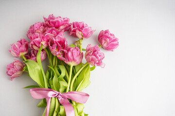 Obraz na płótnie Canvas Bouquet of pink peony tulips tied with a pink bow. Spring flowers on the white background and place for text. Festive concept for Valentines Day or Mother's Day.