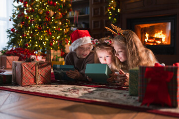 Merry Christmas Xmas holiday. Children unpacking open up gift box near Christmas tree. Kids in...