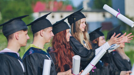 Obraz premium Cheerful graduates pose with raised diplomas on a sunny day.