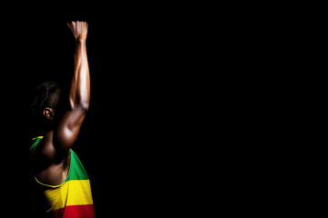 A young African American man in a red, yellow and green T-shirt on a black background raised his hand up. Black History Month - obrazy, fototapety, plakaty