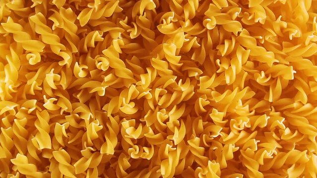 Uncooked Fusilli Pasta - Top View. Fat and Unhealthy Food. Dry Spiral Macaroni, Slowly Rotating Background. Italian Culture and Cuisine. Raw Golden Pasta Pattern. Left Rotation, Low Key Light