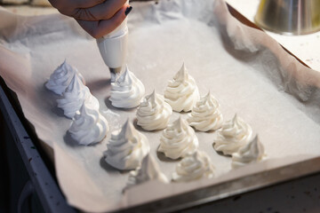 Female hand using piping bag to make meringue cookies in oven tray before baking