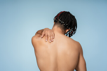 Back view young african american shirtless man holding shoulder wearing stylish dreadlocks on blue background