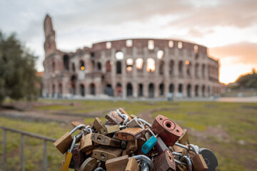 Love padlocks in early morning in front of the colosseum in Rome, red and blue skies with sun just about to rise above the great famous amphitheatre. Autumn setting.