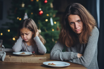 Sad Christmas at home. Upset mother and her little girl sitting at table during Christmas eve dinner. Solitude, loneliness, sorrow, loss, grief, poverty, divorce, conflict, family problems