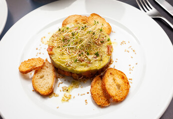 Salmon tartare with guacamole and croutons served on table in restaurant.