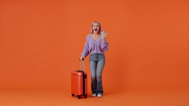Excited woman holding tickets and red suitcase in studio