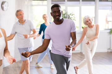 African American man is engaged in modern dance class with group friends of different age and learn...