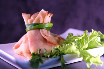 pancake with red caviar and mayonnaise made in a bag tied with green onions on a white square plate Parsley lettuce leaves Ukrainian Slavic food