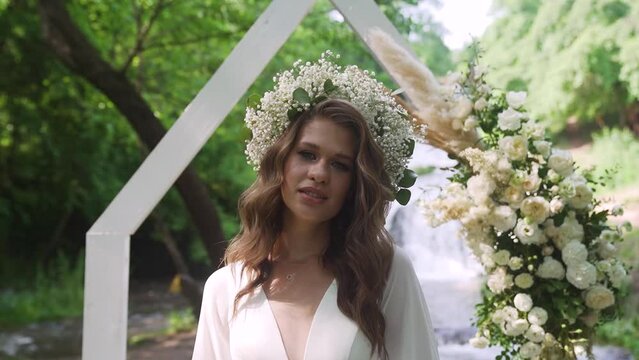 A young woman with flowers wreath walking down near waterfall in the background.