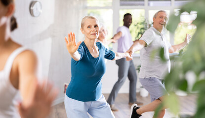 Group of positive adults engaged in dynamic dance in training room during workout session