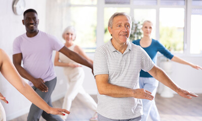 Enthusiastic elderly man practicing modern vigorous dance movements in group dance class with mature people