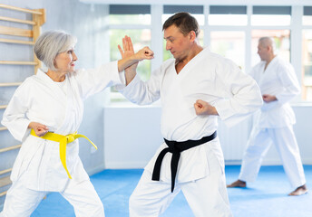 Active middle-aged man attendee of karate classes practicing fighting techniques during workout...