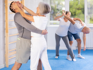 Aggressive old woman practicing self-defense techniques in pairs during workout session