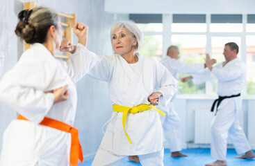 Obraz premium Two elderly women in kimono practice painful blows during karate lessons
