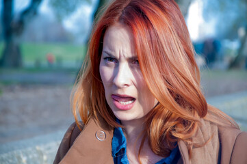 Autumn portrait of a young attractive long haired woman with red hair in the public park
