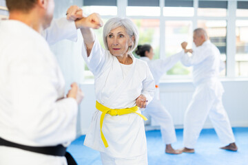 Obraz premium Elderly women and men in pairs exercising karate movements during group training