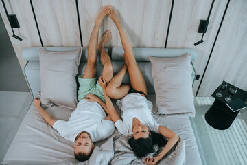 Top view on young couple laying on bed with legs putted on wall relaxing at hotel room. Travel,...