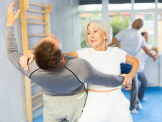 Fototapeta premium Trainer and mature woman train painful hold on self-defense course in a sport gym