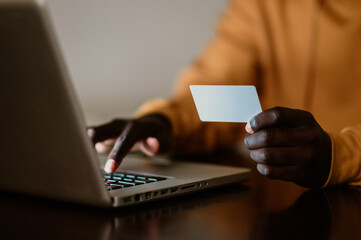 Close up of an african american man using a credit card while typing on a laptop.