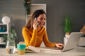 A busy freelancer is using phone and a laptop from home office.