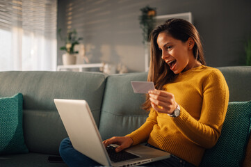 An excited woman is looking at the credit card while using e-banking app.